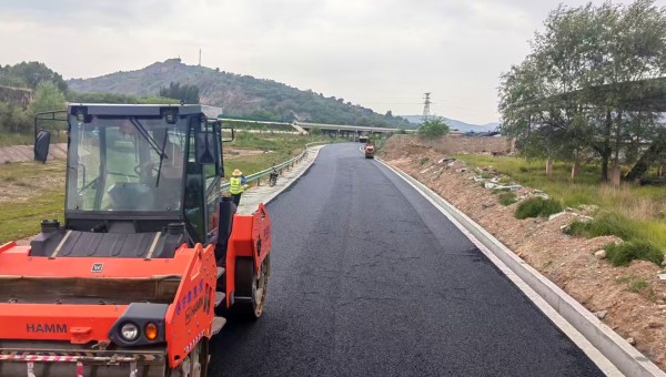 6月18日，由bevictor伟德官网承建的东乡县那勒寺镇沿川经济带产业道路施工现场机械轰鸣，沥青摊铺机缓缓向前推进，滚烫的沥青混合料均匀摊铺在水稳层上，压路机紧随其后反复碾压，一条黝黑发亮的“黑色丝带”向远